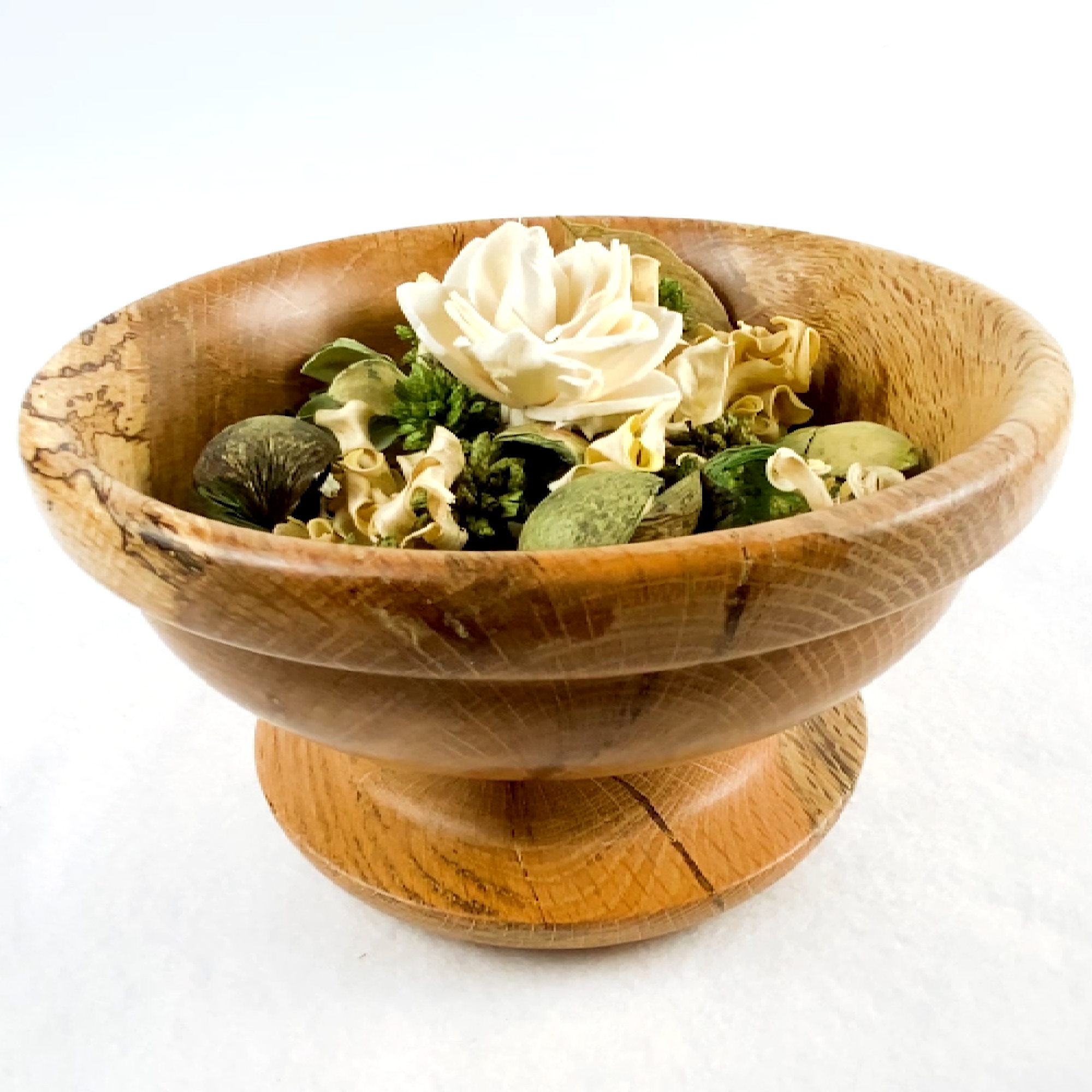 A wooden bowl filled with dried flowers and potpourri on a white background